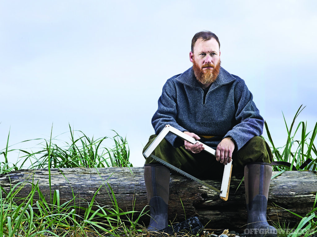 Alone contestant Larry Roberts sitting on a log with a saw.