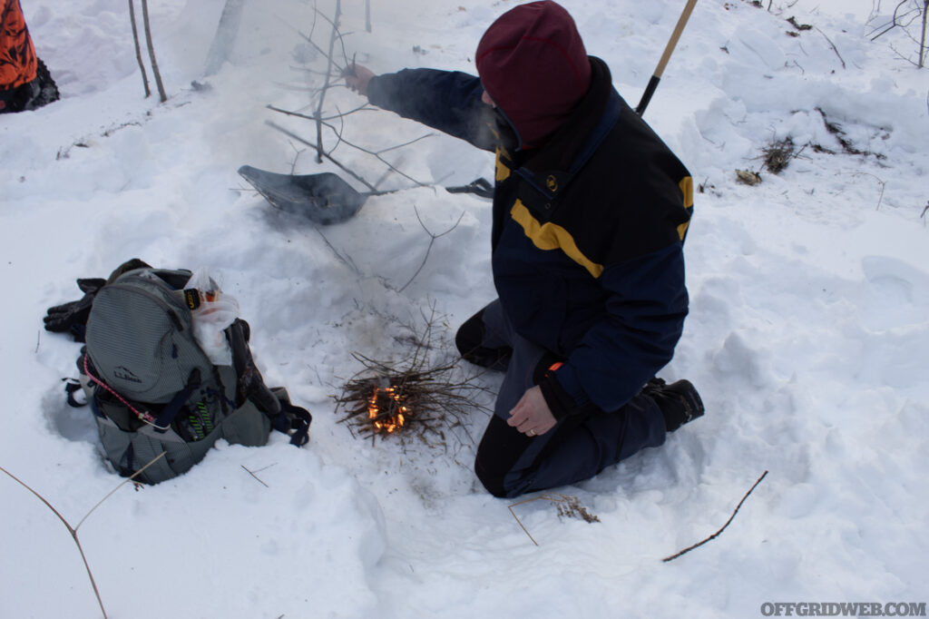 Photo of a winter survival student trying to keep their small fire going in the snow.