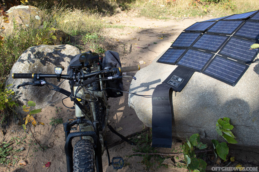 Photo of the QuietKat Warrior eBike parked next to a boulder plugged into its portable solar charger.