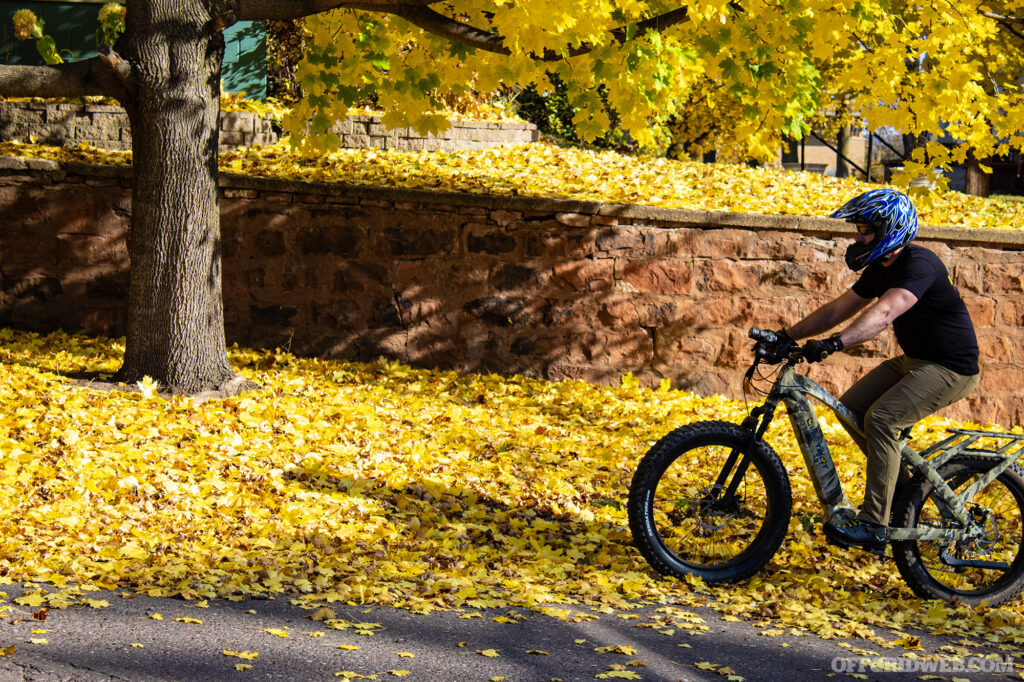 Photo of an adult male riding the Quietkat Warrior through colorful fallen sugar maple leaves on an autumn day.