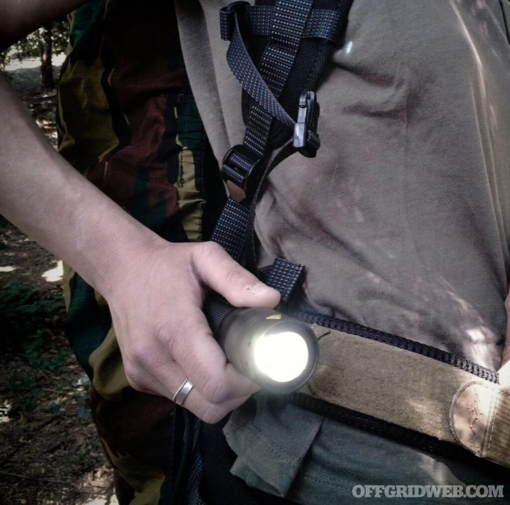 Photo of a handheld led flashlight being held close to the waist while working in the field.