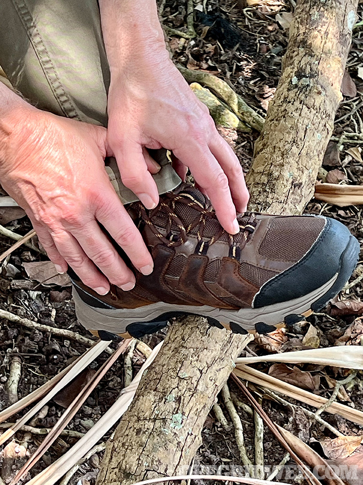 Photo of someone reaching for their boot as the rest their foot on a fallen tree limb.