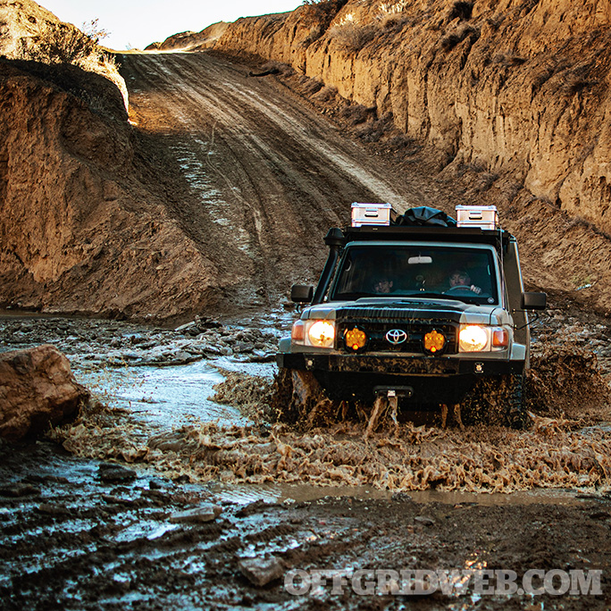 Photo of a Toyota in the middle of a muddy water crossing.