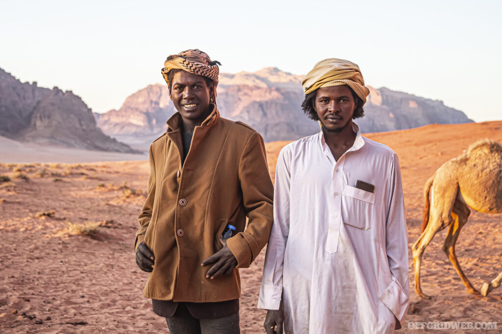 Lifestyle photo of two Jordanian nomads standing in the desert with a camel, and wearing a shemagh, a type of multipurpose survival scarf.