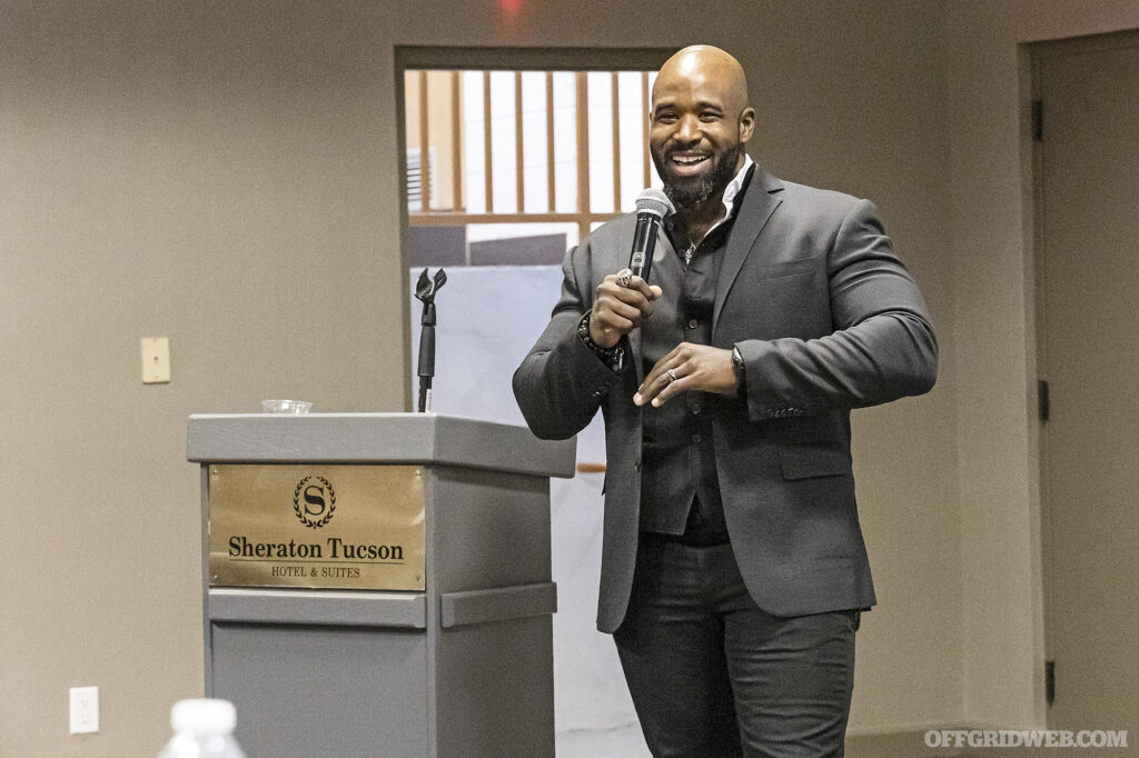 Bryon Rogers gives opening remarks in front of a podium at the Protector Symposium