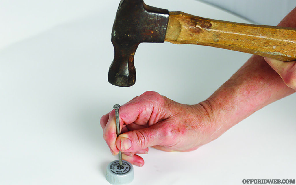 Photo of someone using a hammer and nail to punch several holes into the top of a plastic soda bottle cap.